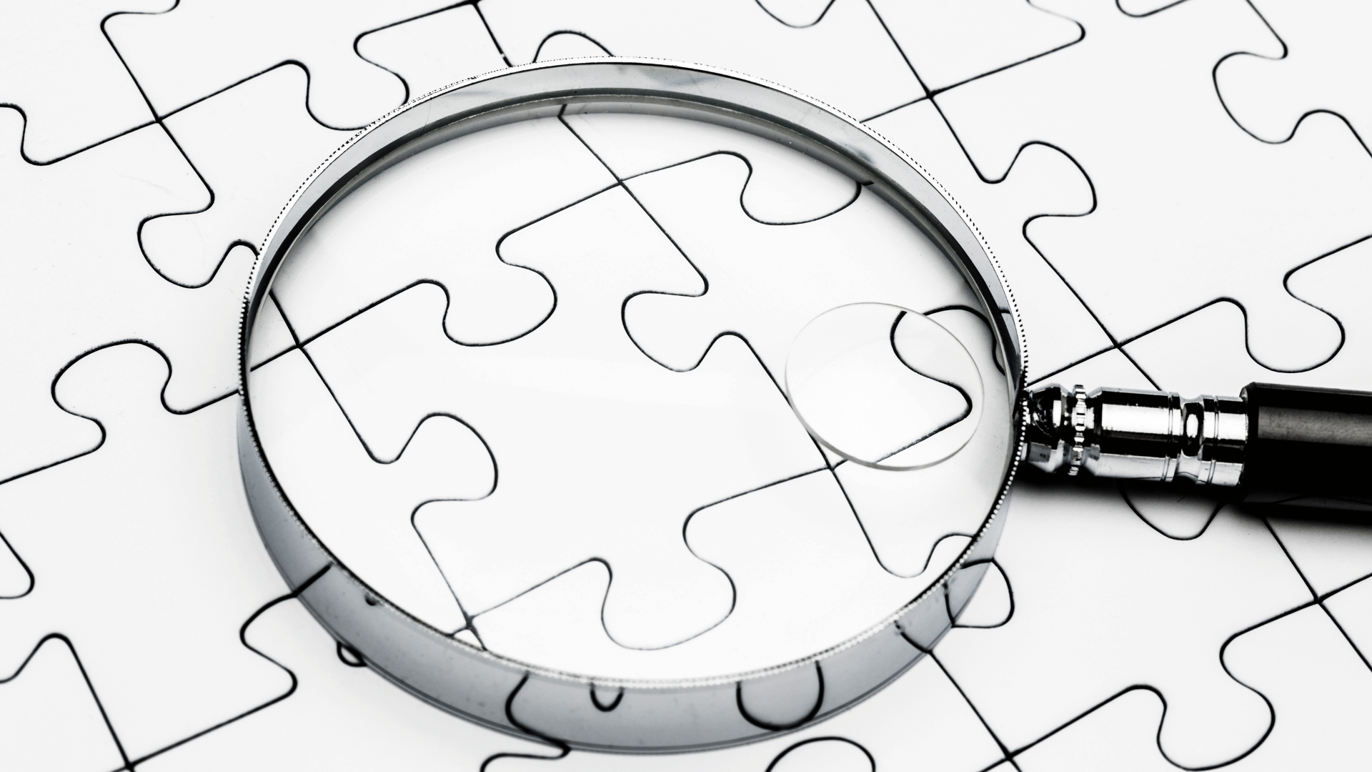 A background display puzzle pieces connected to one another with a magnifying glass placed on the puzzle pieces disconnected